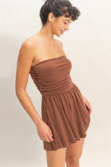 Woman wearing a brown strapless romper against a plain background