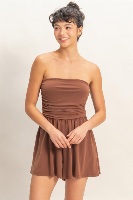 Woman wearing a brown romper dress against a plain background