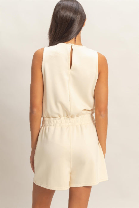 Woman wearing a beige sleeveless romper on a plain background