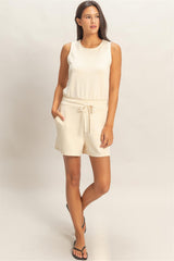 Woman wearing a cream-colored sleeveless romper on a plain background