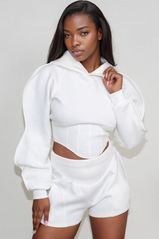 Woman wearing a white hoodie and shorts set against a plain background
