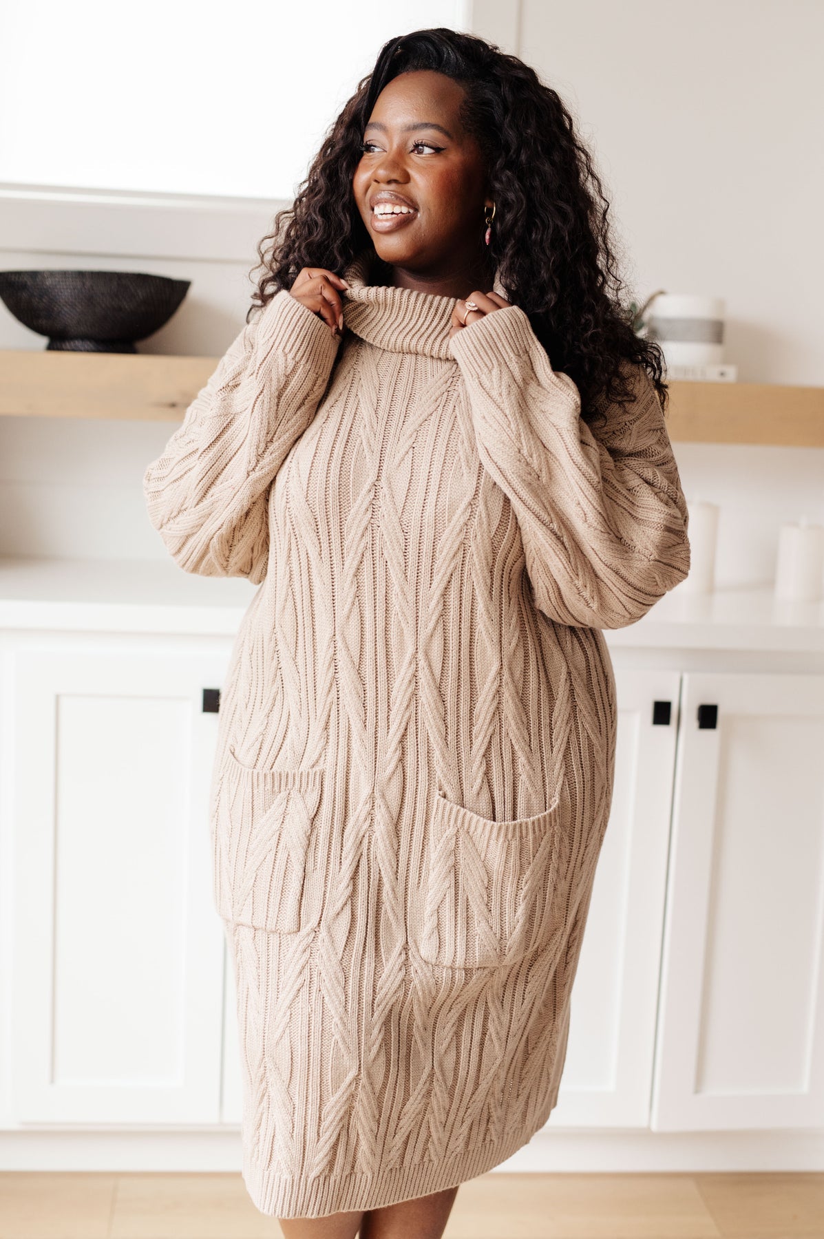 Woman wearing a beige cable knit sweater dress in a kitchen setting