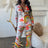 Woman wearing a colorful dragon print pant set in an elegant room with decorative elements.