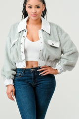 Woman wearing a light gray jacket over a white top and blue jeans on a plain background