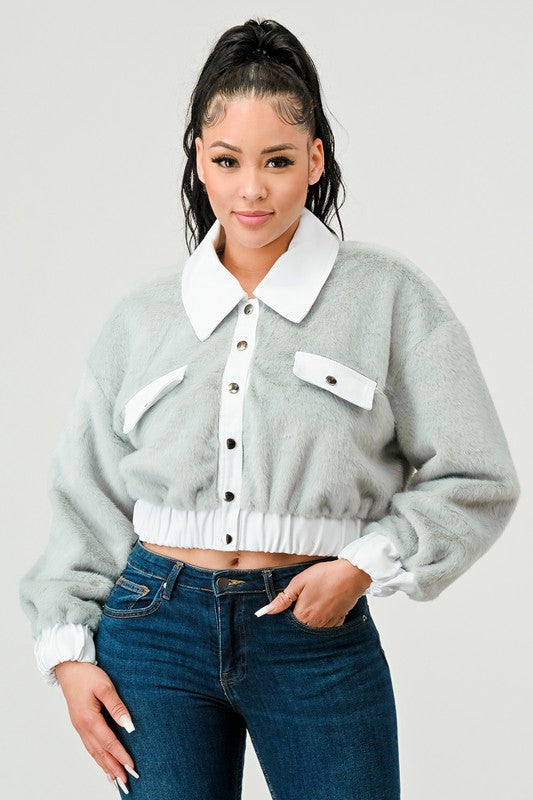 Woman wearing a gray sweater with white collar and buttons, paired with blue jeans on a light gray background