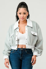 Woman wearing a light gray jacket over a white crop top and blue jeans on a plain background