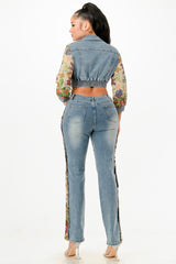 Back view of woman wearing a denim jacket with floral sleeves and light blue jeans on a white background