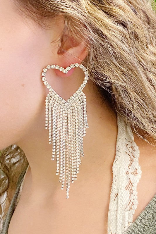 Heart-shaped earring with dangling beads worn by a person with blonde hair.