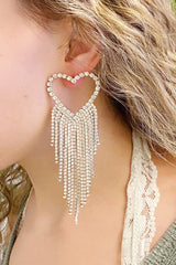 Heart-shaped earring with dangling beads worn by a person with blonde hair.