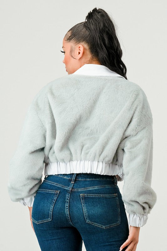 Person wearing a light gray fuzzy sweater and blue jeans on a plain background