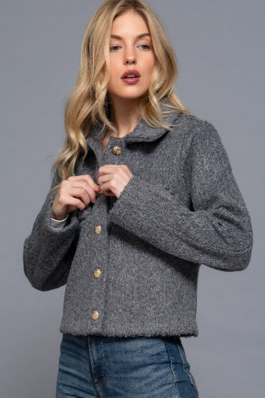 Woman wearing a gray textured jacket with button details on a gray background