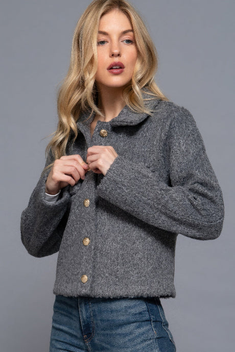 Woman wearing a gray textured jacket with button details on a gray background
