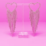 Heart-shaped earrings with dangling crystals on a pink background