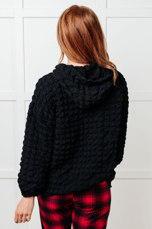 Person wearing a black textured sweater and red plaid pants against a white tiled wall.