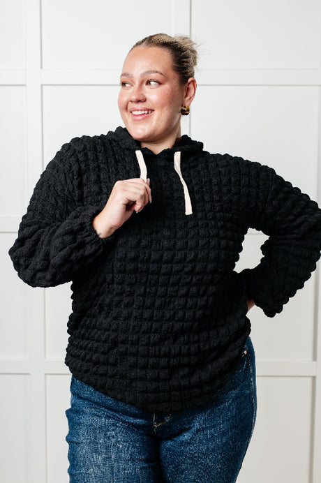 Person wearing a black textured hoodie with a white tiled wall background
