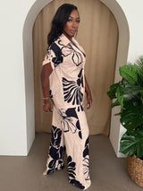 Woman wearing a beige outfit with black floral patterns standing in a room with a plant.