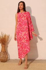 Woman wearing a pink floral dress standing against a white wall.