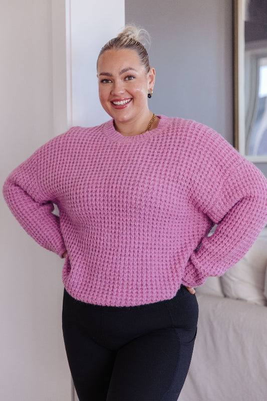 Woman wearing a pink sweater standing indoors.