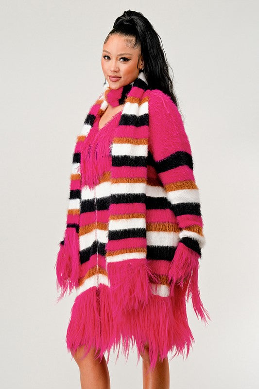 Person wearing a bright pink fringe cardigan with a colorful striped scarf on a light gray background