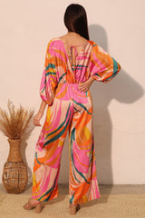 Woman wearing a colorful patterned jumpsuit standing against a plain wall. back view