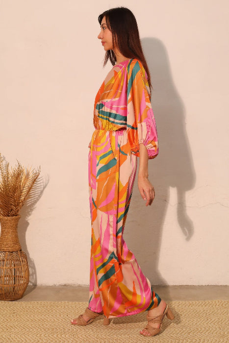 Woman wearing a colorful pink jumpsuit standing against a plain wall with a woven basket in the foreground. side view