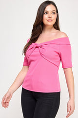 Woman wearing a pink off-shoulder top with a knot detail on a white background