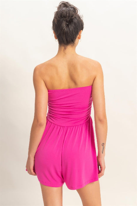 Woman wearing a bright pink strapless romper on a plain background
