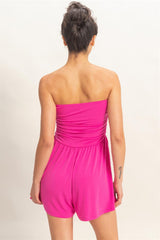 Woman wearing a bright pink strapless romper on a plain background