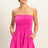 Woman wearing a bright pink strapless romper against a plain background
