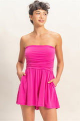Woman wearing a bright pink strapless romper against a plain background