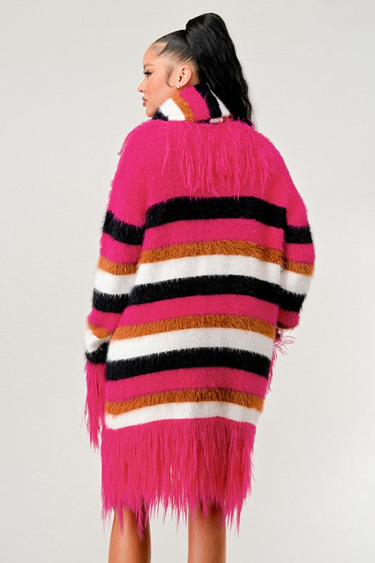 Woman wearing a colorful striped sweater with fringe details on a plain background