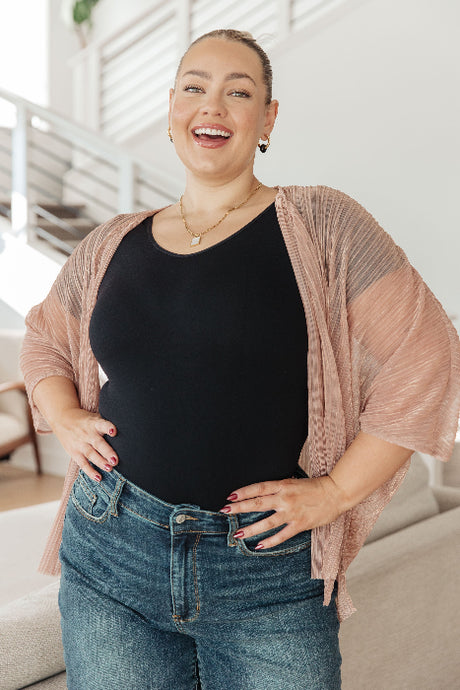 Woman wearing a black top and blue jeans with a pink cardigan indoors.