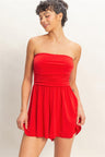 Woman wearing a strapless red romper against a plain background