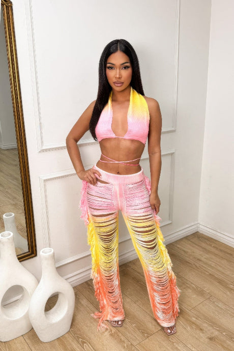 Woman wearing a colorful tie-dye outfit in a room with white walls and wooden floor.