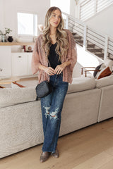 Woman in a pink cardigan, black top, and blue jeans standing in a modern living room.