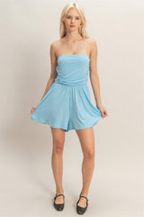 Woman wearing a light blue strapless romper on a plain background