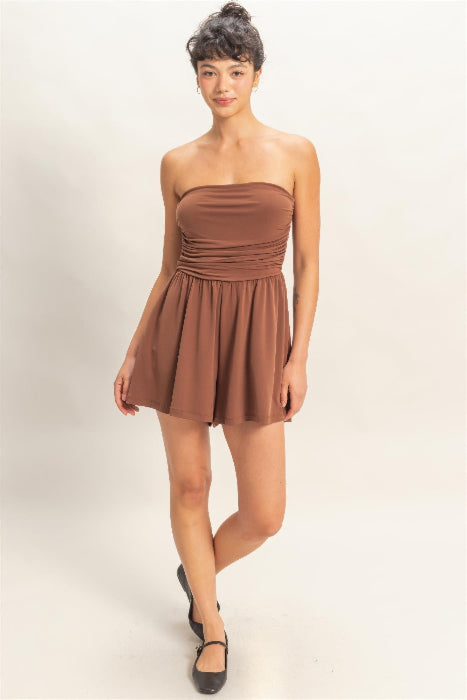 Woman wearing a brown strapless romper on a plain background