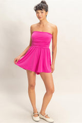 Woman wearing a bright pink strapless romper on a plain background