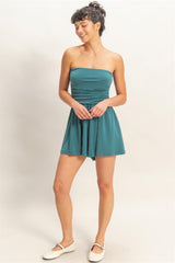 Woman wearing a teal strapless romper on a plain background