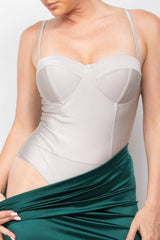 Woman wearing a silver corset top and green skirt against a plain background