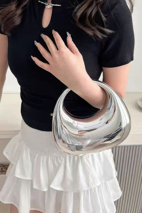 Person holding a silver handbag with a black top and white skirt.