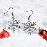 Silver snowflake earrings with red ornaments on a snowy background