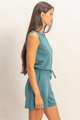 Woman wearing a teal sleeveless romper against a plain background