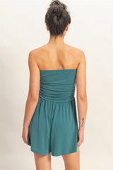 Woman wearing a teal strapless romper on a beige background