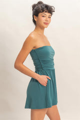 Woman wearing a teal strapless romper against a plain background