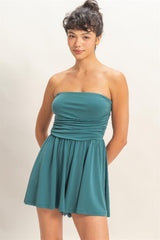 Woman wearing a teal strapless romper on a plain background