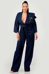 Woman wearing a dark denim jumpsuit with ruffled details on a white background