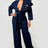 Woman wearing a dark denim blue jumpsuit with ruffled details on a white background