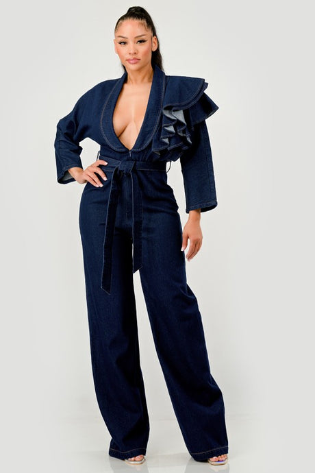 Woman wearing a dark denim blue jumpsuit with ruffled details on a white background