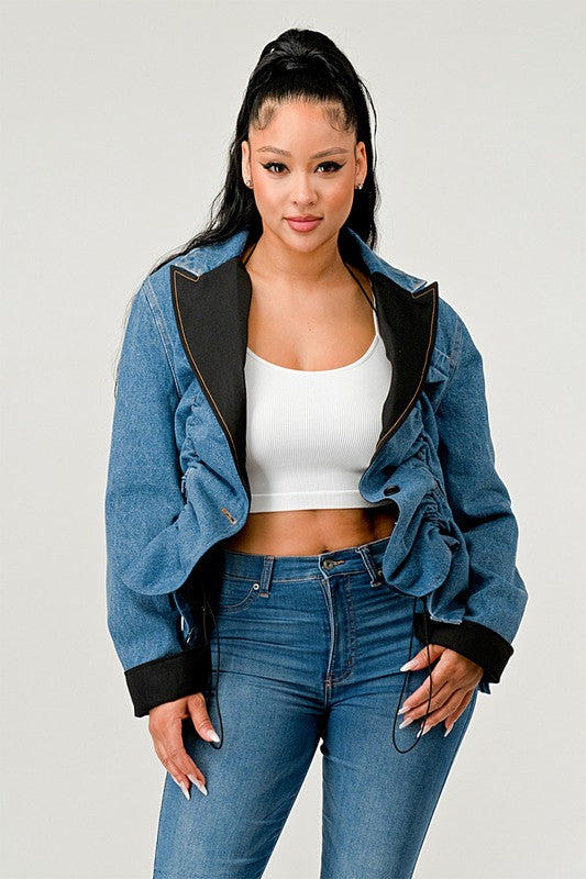 Woman wearing a denim jacket with black trim and high-waisted jeans on a plain background